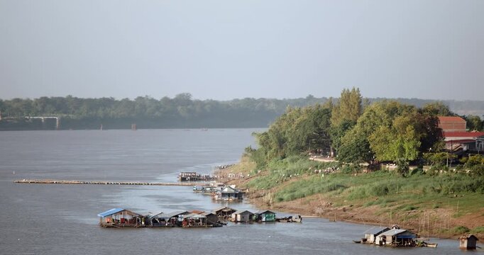 People disembarking from a ferry to reach the street along the Mekong riverbank featuring floating houses and a bamboo bridge.