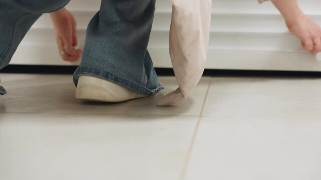 Low angle view of laundry worker sliding up entrance door to laundry room, denim jeans and white sneakers visible on tile floor, bright indoor service setting, clean modern corridor backdrop