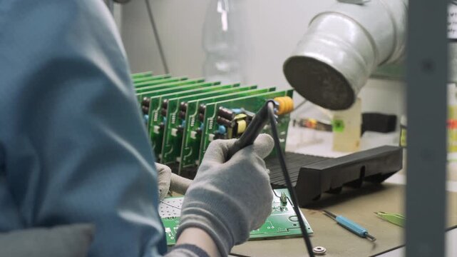 Close-up shot of a female's hands in a protective gloves. Woman technician engineer soldering circuit board in laboratory. Electronics service technology.