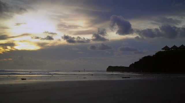 Wide view of Kelating Beach at dusk with cliff, Balinese gazebos