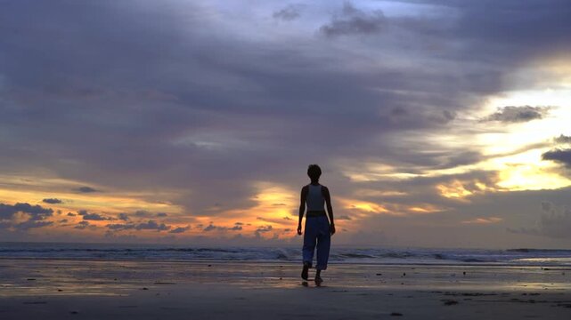Woman strolling on Kelating Beach and looking at ocean at sunset