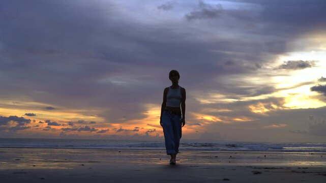 Woman strolling on Kelating Beach and looking at ocean at sunset