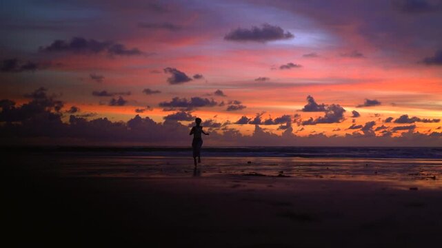 Woman running on Kelating Beach at vivid pink and orange sunset
