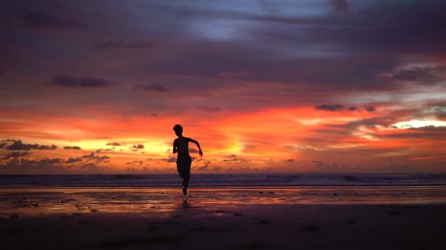 Woman running on Kelating Beach at vivid pink and orange sunset