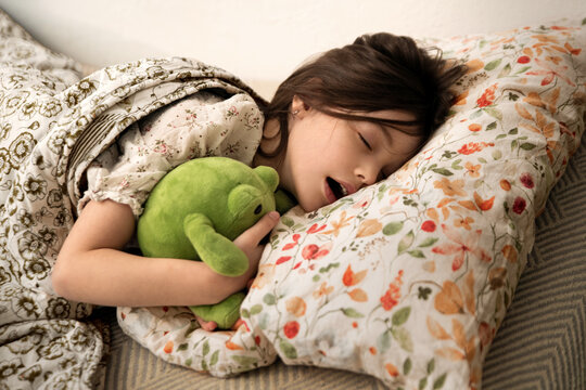 Kid girl sleeping in bed with plush frog toy. on floral pillow
