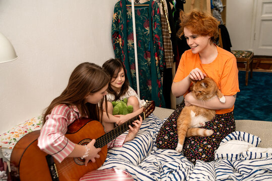 mother with two daughters and cat are playing guitar on bed