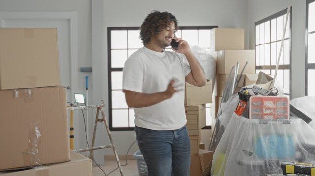Man on smartphone pointing to stacked cardboard boxes in a new building; planning moving organization.