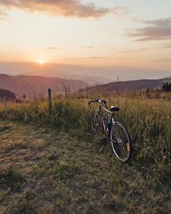 Fototapeta premium Serene Mountain Landscape at Sunset with a Bicycle Resting in Tall Grass, Golden Hour Light