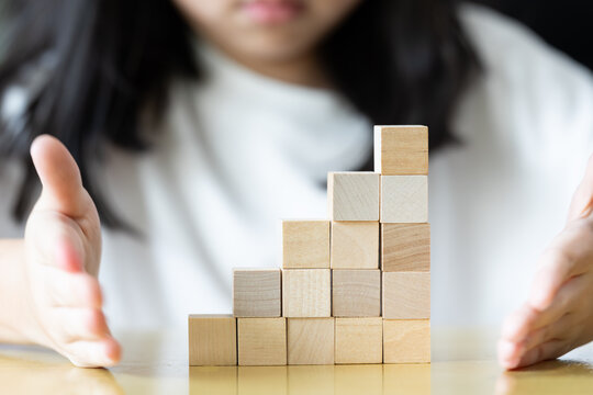 oth hands hold a wooden block tower as small fingers slowly adjust and place pieces one by one on a rug keeping the structure upright neat and stable through careful practice.