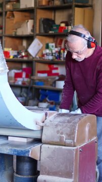 Senior carpenter sanding wooden parts with machinery