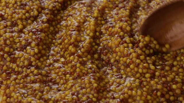  close up grainy mustard mixing with wooden spoon