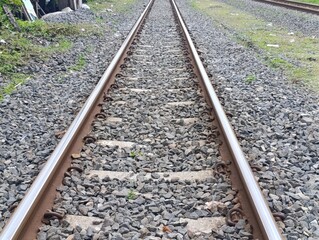 Fototapeta premium Railway tracks extending into the distance, gravel ballast, and green grass.