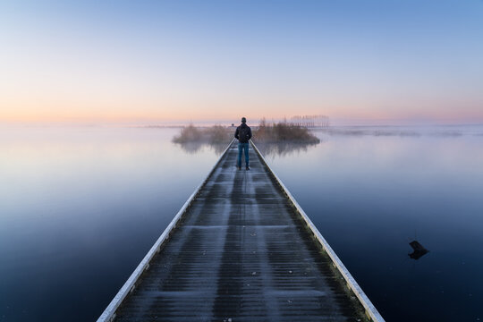 A man on a small bridge enjoying a foggy, spring dawn in a nature area.