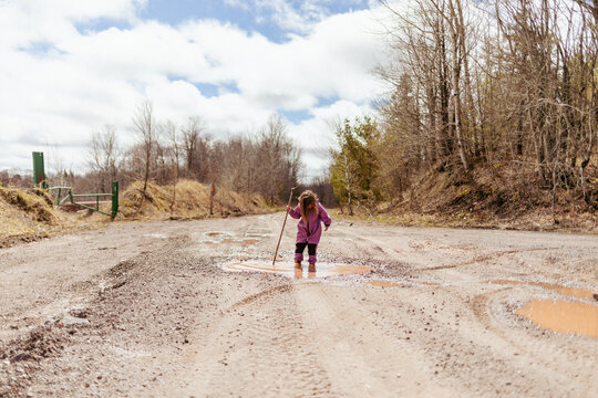 Child in rainsuit splashing in puddle with walking stick