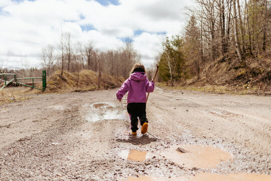 Little girl running through muddy spring puddles