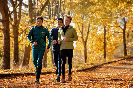 Three teenage boy athlete jogging through autumn park.