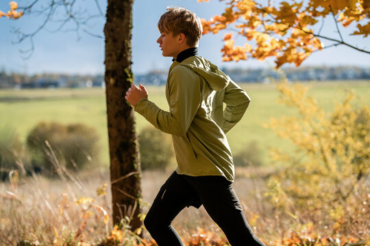 Teenage boy jogging in autumn park. Young runner training on nature