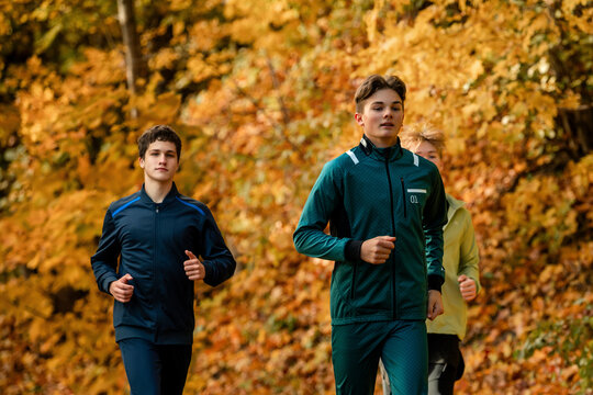 Group of teenage boy runners jogging along a path in autumn forest.