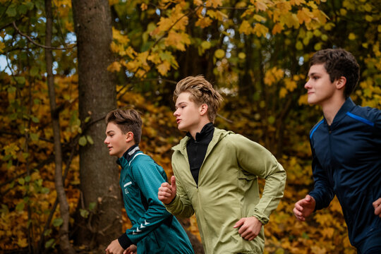 Group of teenage boy runners jogging along a path in autumn forest.