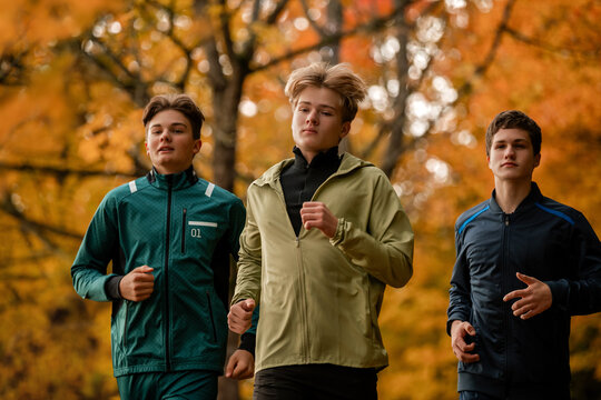 Group of teenage boys jogging through autumn park.