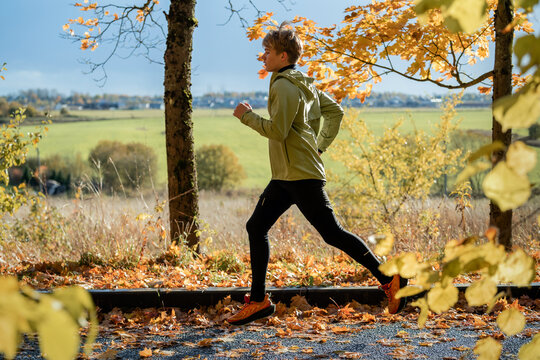 Teenage boy jogging in autumn park along leaf-covered path