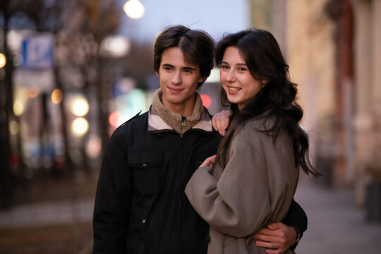 Couple embracing and smiling in city street during evening.