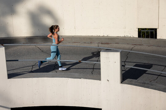 Athletic 30 year old woman running in a parking structure at sunset