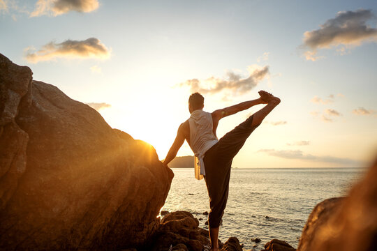 A guy standing with his back to the camera at sunset doing an asana