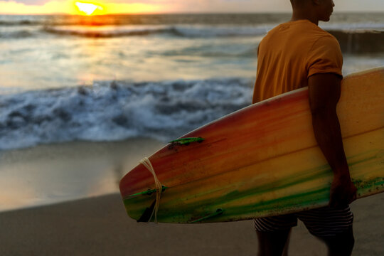 A guy with a surfboard at sunset by the ocean