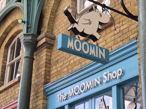 London UK 04.07.2025 Moomin shop sign with cartoon character hanging on brick wall inside covered market arcade with steel columns and decorative lights showcasing playful retail storefront