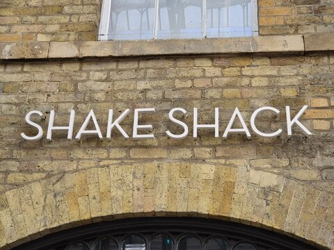 London UK 04.07.2025 Shake Shack sign mounted on brick wall above arched entrance inside historic market arcade showcasing iconic fast food brand in urban retail environment