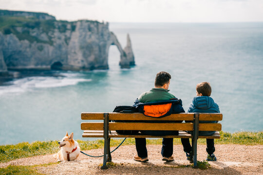 Dad and son enjoy time together on bench, corgi dog rests in Etretat