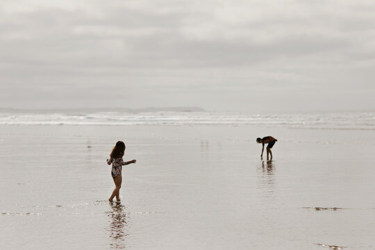 Two young children playing in the shallow water on a wide sandy beach