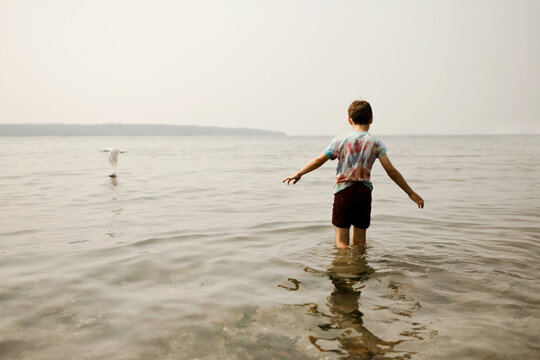 Young boy in a tie-dye shirt standing in calm ocean water at the beach
