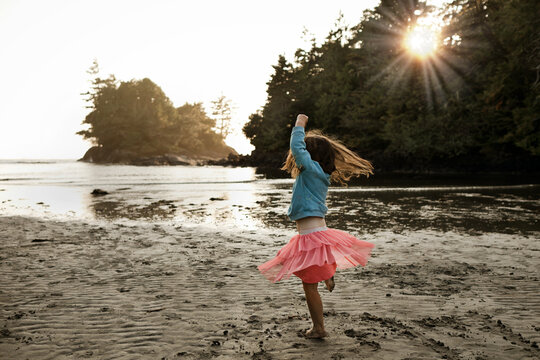 Young girl dancing on a sandy beach looking at the ocean at dusk