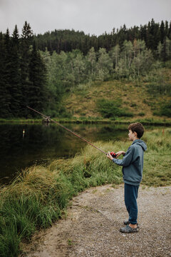 Young boy in a blue hoodie fishing by a calm lake in a forest