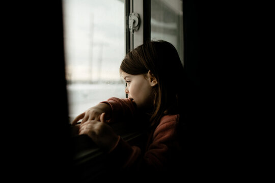Young Caucasian girl looking out of a window in a dark room