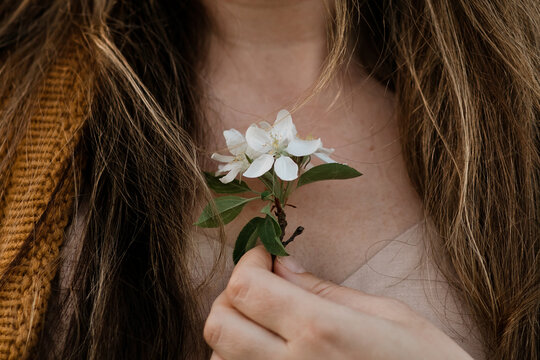 Close up of a woman holding a white spring blossom against her chest
