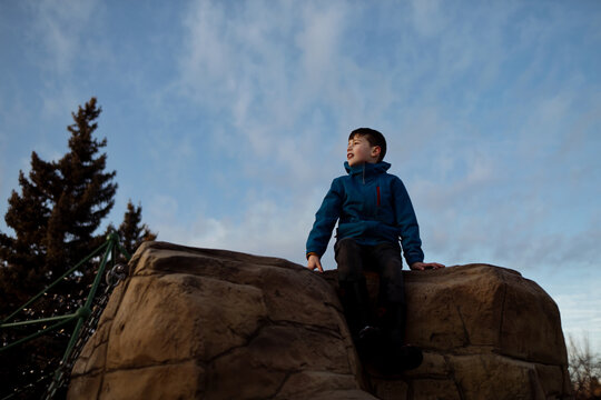 Young boy sitting on a large rock climbing structure at a park
