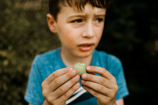 Young boy holding a small green apple with a bite taken out outdoors