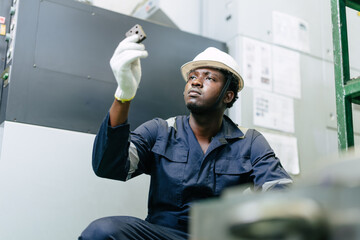 Young African black male worker in safety dress hardhat look at workpiece focused and determined.