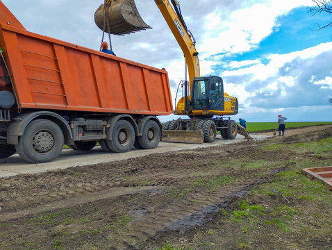 Lviv region, Ukraine - April 09, 2026: A powerful JCB wheeled excavator works in coordination with a large orange dump truck on rural road reconstruction.