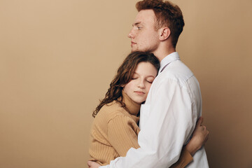 Fototapeta premium Young couple embraces tenderly with eyes closed against beige background. Intimate moment of affection and comfort, expressing love, trust, and emotional connection between partners.