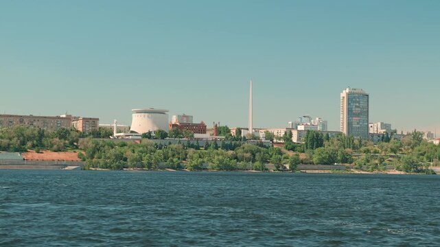 Wide cityscape of Volgograd from the Volga River. The panorama shows the Battle of Stalingrad museum and monument on the green embankment. Clear summer day with calm water and retro colors