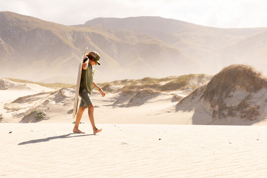 10 year old boy carrying sand board on sand dunes, Walker Bay Nature Reserve, Stanford, South Africa