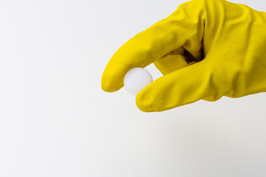 Hand in Yellow Rubber Glove Holding Single White Mothball on White Background