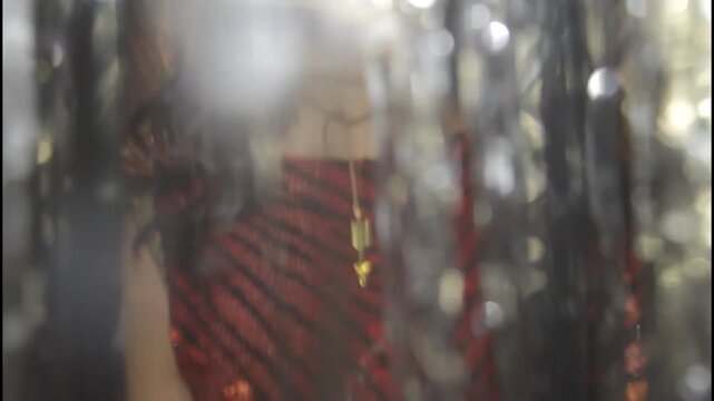 A woman in a shiny dress stands in silhouette against a curtain
