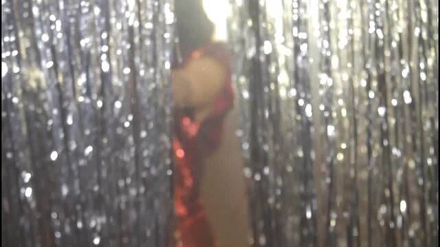 A woman in a shiny dress stands in silhouette against a curtain
