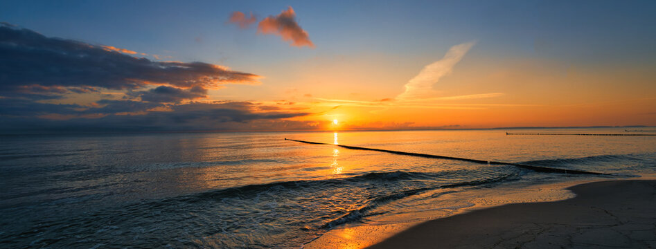 Panoramic sunrise over the Baltic Sea beach with wooden groynes and golden reflections on the water - authentic - Golden sunrise over the ocean - concept for new beginnings, hope and future