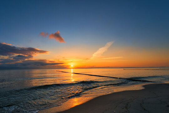 Golden sunrise over the Baltic Sea beach with wooden groynes and orange sky, Usedom island, Germany
